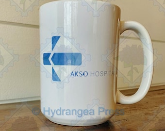Puede incluir: Taza de cerámica blanca con un logotipo azul y blanco que dice "AKSO HOSPITAL" y "Hydrangea Press".