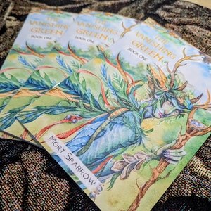 May include: Three copies of "The Vanishing Green Book One" by Mort Sparrow. The book cover shows a watercolour illustration of a forest spirit with antlers, holding a staff. The background is a mix of green, blue, and brown tones.