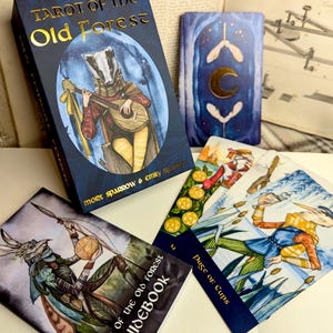 May include: Tarot of the Old Forest deck with a guidebook, featuring a blue and gold card with a badger playing a lute. The card is surrounded by other cards, including the Page of Cups.