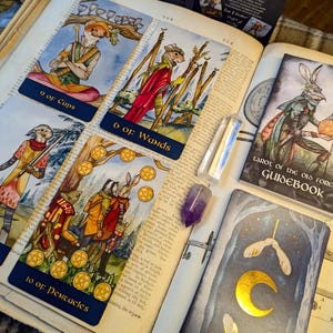 May include: A set of three tarot cards from the "Tarot of the Old Forest" deck. The cards are 9 of Cups, 6 of Wands, and 10 of Pentacles. Each card features a whimsical illustration of woodland creatures in a forest setting. The cards are printed on thick cardstock with a blue border and gold accents.