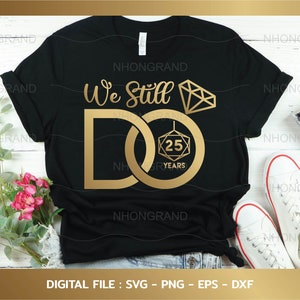 May include: A black t-shirt with the text "We Still Do" in gold lettering. The "D" is formed by two interlocking gold rings, one with a diamond and the other with a 25th anniversary inscription.