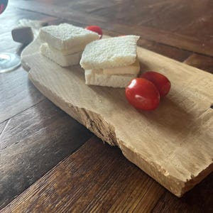 Peut inclure: Une planche de service en bois rustique avec deux petits sandwichs et trois tomates cerises rouges. Les sandwichs sont faits avec du pain blanc et une garniture de couleur claire. La planche a un bord naturel et non fini.