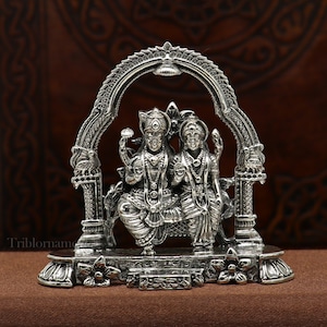 May include: Silver statue of a Hindu deity couple, Shiva and Parvati, seated together under an archway. The statue is intricately detailed and has a traditional Indian design.