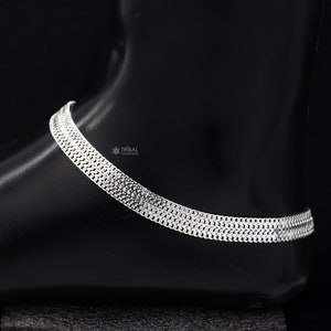 May include: Silver anklet with a layered chain design. The anklet is made of multiple strands of silver chain that are linked together to create a thick, layered look. The anklet is shown on a black background.