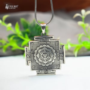 Könnte beinhalten: Eine silberne Halskette mit einem quadratischen Anhänger, der mit komplizierten Gravuren und Sanskrit-Text verziert ist. Der Anhänger zeigt eine stilisierte Blume mit einem Stern in der Mitte. Der Text enthält die Wörter "Ganapataye Namah", "Kshetrapalaya Namah", "Batukaaya Namah" und "Yogini Namah".