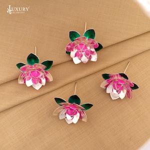 Puede incluir: Cuatro pares de pendientes de plata con forma de flor de loto. Cada pendiente presenta pétalos rosas y blancos con hojas verdes. Los pendientes se muestran sobre un fondo de tela beige. El texto "LUXURY SILVER GIFT" está en la esquina superior izquierda.