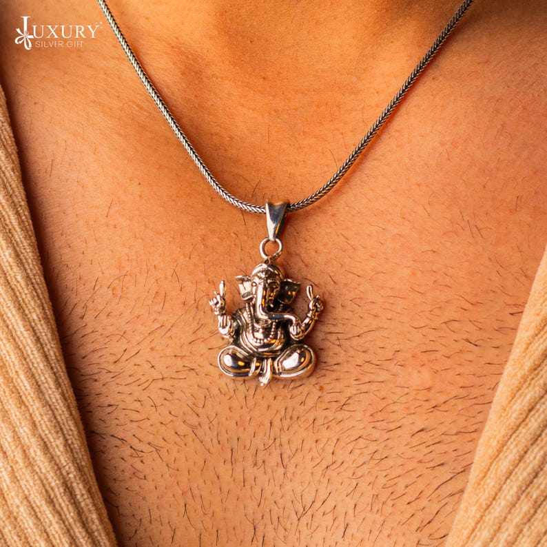May include: A silver chain necklace with a silver pendant featuring a detailed depiction of the Hindu deity Ganesha.