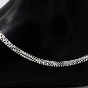 May include: A silver anklet featuring a delicate, layered chain design. The anklet is crafted from small, round beads linked together in a repeating pattern.