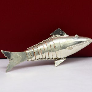 May include: A silver fish shaped decorative object. The fish is detailed with scales and fins.