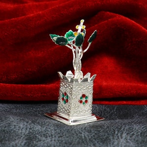 Puede incluir: Una figurita de planta Tulsi de plata con hojas de esmalte verde y amarillo, de pie sobre una base de plata con acentos de esmalte rojo y verde.