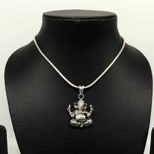 May include: A silver chain necklace with a pendant featuring a detailed depiction of the Hindu deity Ganesha. The pendant is a three-dimensional representation of Ganesha sitting in a meditative pose.