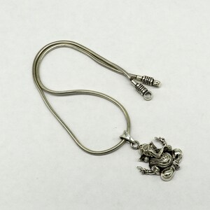 May include: A silver chain necklace with a silver pendant featuring a detailed depiction of the Hindu deity Ganesha. The chain is a snake chain style.
