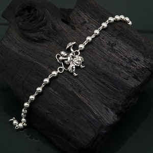 May include: A silver charm bracelet featuring a small, detailed charm of a person holding an umbrella. The bracelet is made of small, round beads.