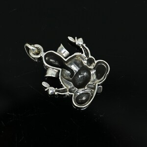 May include: A silver charm in the shape of a cartoon character with black enamel details. The charm has a loop for attaching to a bracelet or necklace.