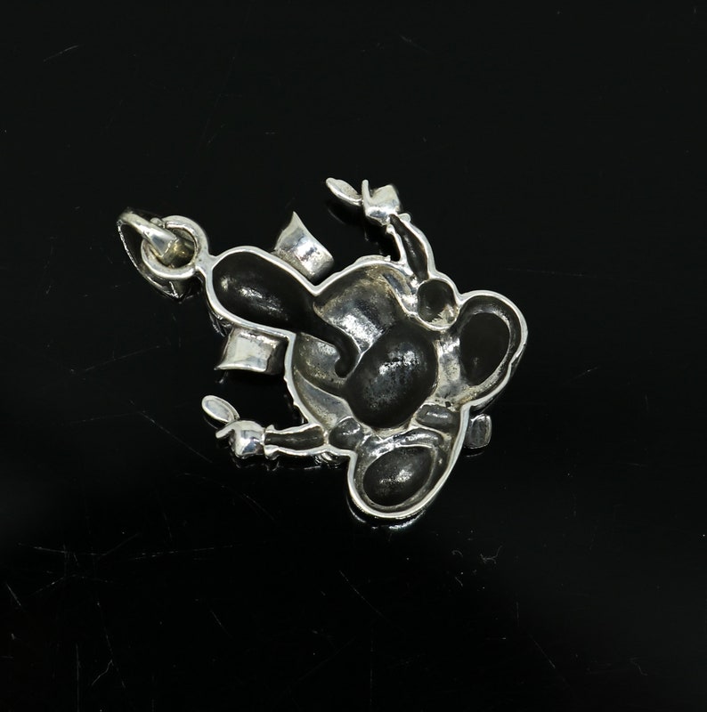 May include: A silver charm in the shape of a cartoon character with black enamel details. The charm has a loop for attaching to a bracelet or necklace.