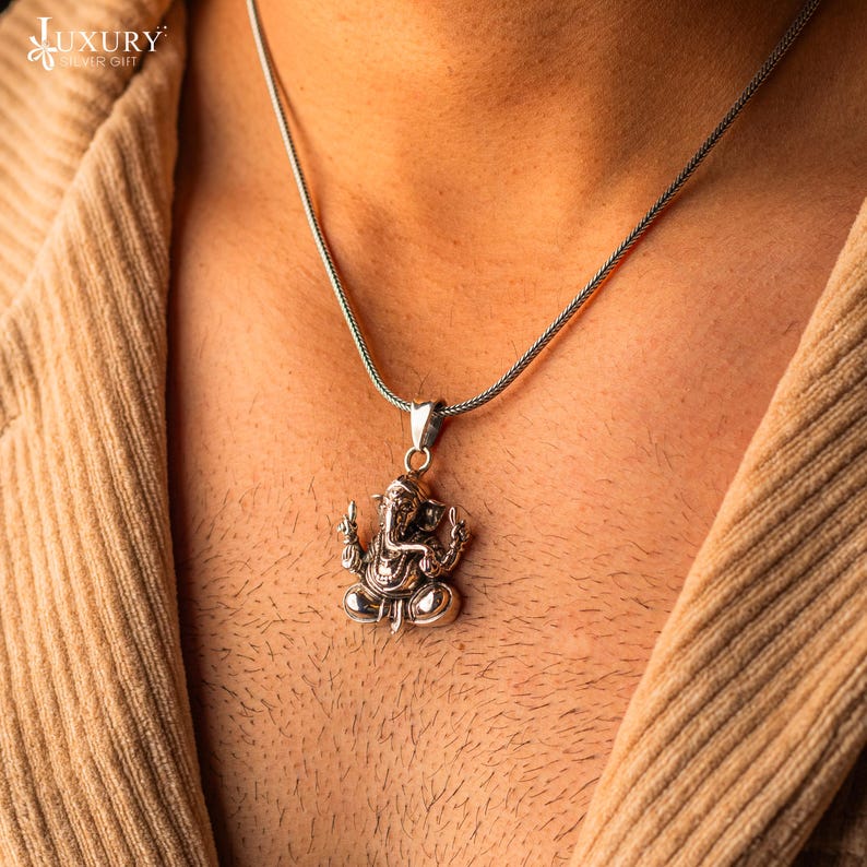 May include: A silver chain necklace with a silver pendant featuring a detailed depiction of the Hindu deity Ganesha.