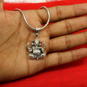 May include: Silver chain necklace with a detailed silver pendant of the Hindu deity Ganesha. The pendant features Ganesha sitting with his trunk raised and his hands in a gesture of blessing.