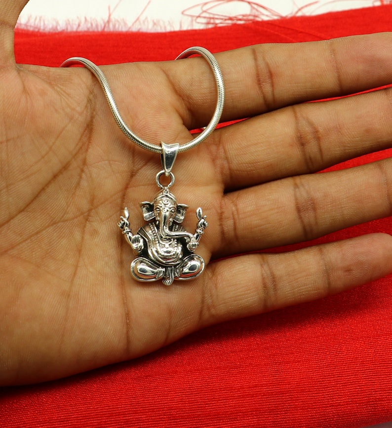 May include: Silver chain necklace with a detailed silver pendant of the Hindu deity Ganesha. The pendant features Ganesha sitting with his trunk raised and his hands in a gesture of blessing.