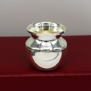 Puede incluir: Una olla redonda decorativa de plata con una superficie lisa y brillante. La olla está sobre una superficie roja.