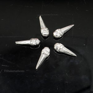 May include: Five silver metal pendants shaped like teardrops with a textured design. The pendants are arranged in a star shape on a black background.