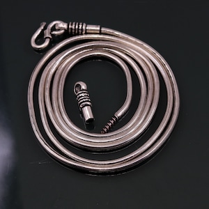 Op de afbeelding: Een zilveren slangenketting met een zilveren sluiting. De ketting is opgerold en ligt plat op een zwart oppervlak.