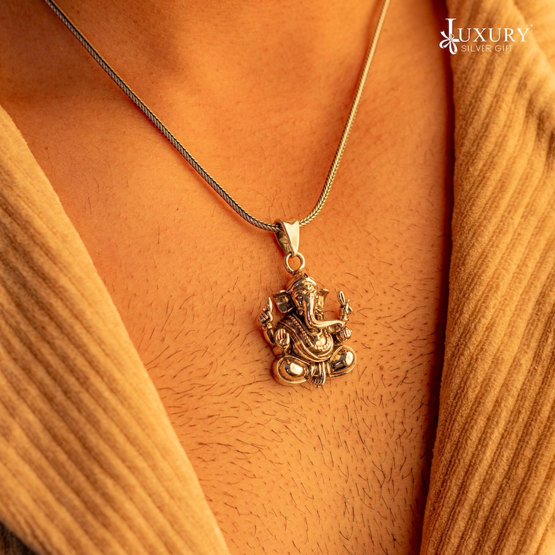 May include: A silver chain necklace with a detailed silver pendant of the Hindu deity Ganesha. The pendant is intricately sculpted and features the elephant head and trunk of Ganesha.