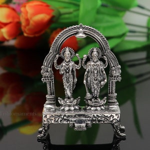 May include: Silver statue of two Hindu deities standing on lotus pedestals under an archway. The statue is intricately detailed and has a traditional design.