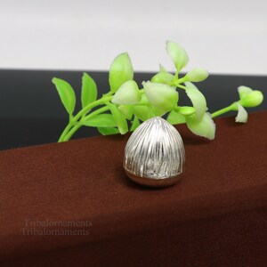 May include: A silver, egg-shaped, decorative object with a textured surface. The object is sitting on a brown surface.