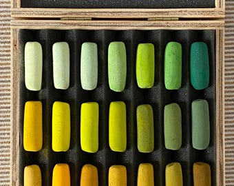 May include: A wooden box containing twenty-one rectangular pastel sticks arranged in three rows of seven, featuring a gradient of yellow, orange, and green shades. The lid interior displays a white card with the text: THIS BOX IS NUMBER _ OF A LIMITED EDITION OF _ BOXES. THIS PASTEL SET WAS HANDCRAFTED ON _ OF YEAR _.