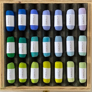 Könnte beinhalten: Eine Holzkiste mit 20 weichen Pastellkreiden in verschiedenen Farben, darunter Blau, Grün, Gelb und Lila. Jede Pastellkreide hat ein weißes Etikett mit dem Text "MAMUT". Die Pastellkreiden sind in Reihen in einer schwarzen Schaumstoffeinlage angeordnet.