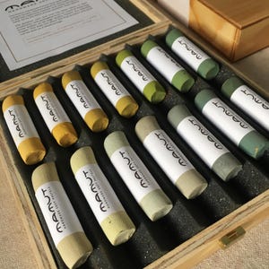 Peut inclure: Une boîte en bois remplie d'un ensemble de 15 bâtonnets de pastel. Les bâtonnets sont disposés en rangée et sont étiquetés avec le mot "MAMUT" et la phrase "PASTELS DOUX FAITS MAIN".