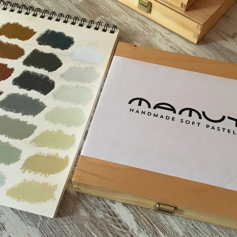 以下が含まれることがあります： 「MAMUT HANDMADE SOFT PASTEL」と書いてある白いラベルが付いた木製の箱。箱が開いていて、さまざまなパステルカラーが見えます。