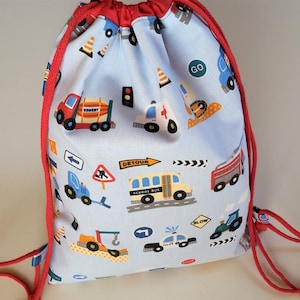 Op de afbeelding: Een blauwe trekkoordtas met een rood trekkoord. De tas is versierd met een patroon van verschillende voertuigen, waaronder een schoolbus, een brandweerwagen, een politieauto en een bouwvoertuig. De tekst "DETOUR" en "SCHOOL BUS" is zichtbaar op de tas.