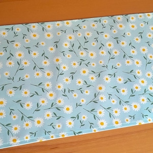 Könnte beinhalten: Ein hellblauer Stoff mit einem weißen Gänseblümchenmuster. Der Stoff ist glatt und hat einen dezenten Glanz.