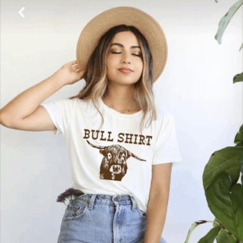 May include: White t-shirt with a brown Highland cow illustration and the text "BULL SHIRT" printed on the front.