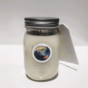 May include: A white soy wax candle in a clear glass jar with a silver lid. The jar has a label with a blue and green globe and the text "Yahweh is the Creator". The text "In the beginning God created the heavens and the earth" is also on the label.
