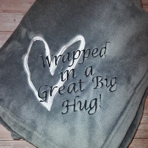 May include: Gray fleece blanket with white embroidered heart and the text "Wrapped in a Great Big Hug!"