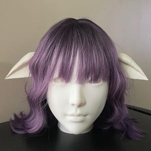 May include: A white mannequin head with purple and white wavy hair, wearing elf ears.
