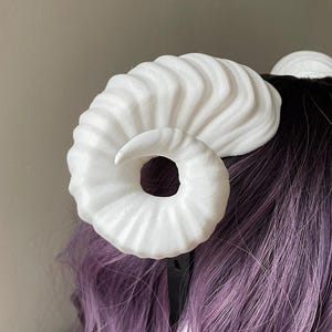 Close up of a 3D printed white ram horn mounted to a black headband displayed on a mannequin
