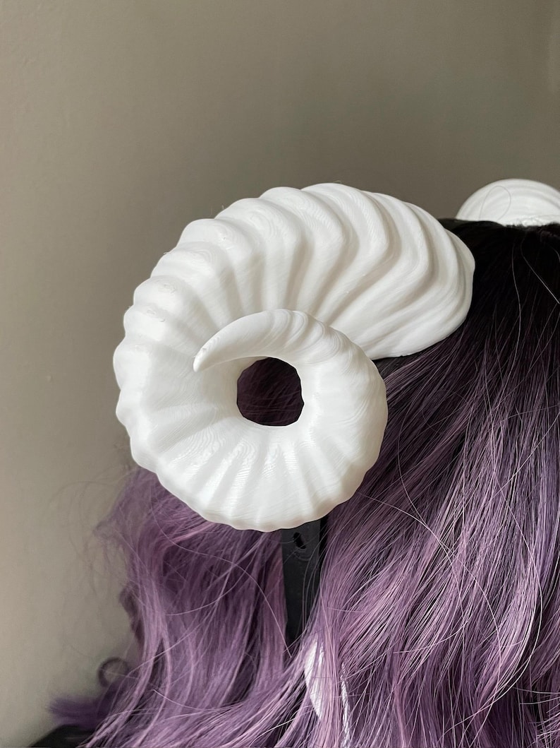 Close up of a 3D printed white ram horn mounted to a black headband displayed on a mannequin