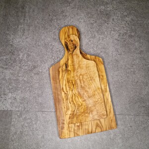 Op de afbeelding: Twee snijplanken van olijfhout. De planken zijn in elkaar geschoven, met de kleinere plank bovenop de grotere plank. De planken hebben een natuurlijke houtnerf en zijn lichtbruin.