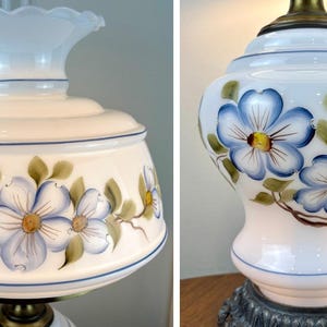 May include: A white glass lamp with a blue and yellow floral design. The lamp has a white shade with a scalloped edge and a brass base.