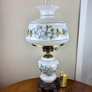 May include: White ceramic lamp with a blue and green floral design. The lamp has a white shade with a scalloped edge and a brass base.