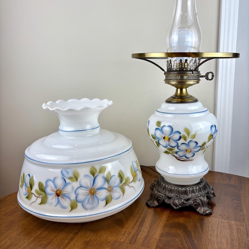 May include: A white glass lamp with a blue and green floral design. The lamp has a white glass shade with a scalloped edge and a brass base.