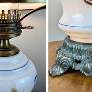 May include: A white ceramic lamp with blue floral designs and a gold metal base. The lamp has a clear glass shade and a metal finial.