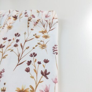 May include: White fabric with a floral pattern featuring brown and pink wildflowers. The fabric has a subtle texture.