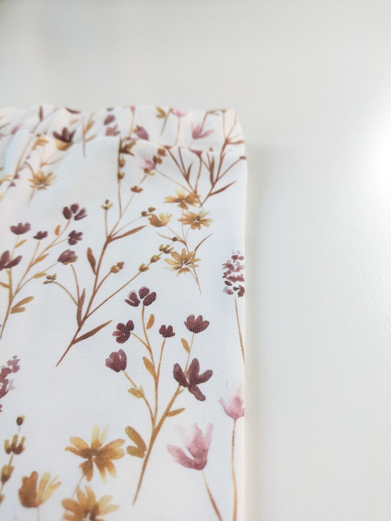 May include: White fabric with a floral pattern featuring brown and pink wildflowers. The fabric has a subtle texture.