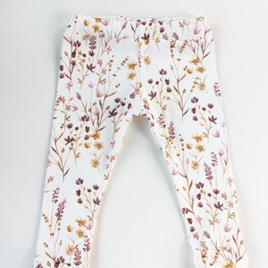 May include: White leggings with a floral print featuring brown, pink, and yellow flowers.