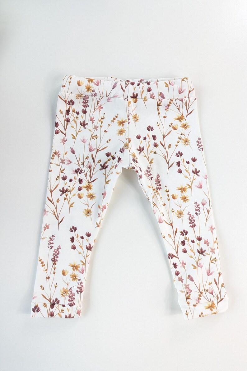 May include: White leggings with a floral print featuring brown, pink, and yellow flowers.