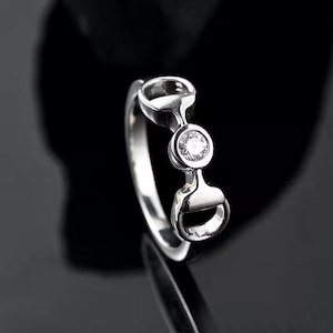 Könnte beinhalten: Ein silberner Ring mit einem einzelnen klaren Diamanten, der in einem Hufeisen-Design gefasst ist.